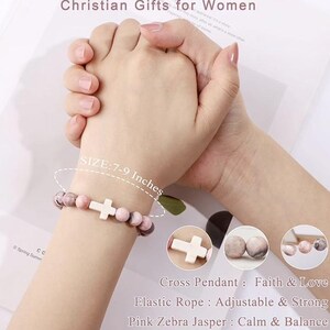 May include: A pink and white beaded bracelet with a white cross charm. The bracelet is made with elastic rope and pink zebra jasper beads. The bracelet is 7-9 inches in size.