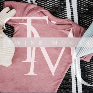 May include: A dusty rose baby onesie with a white "Twin" logo on a black and white striped background.