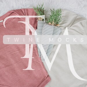May include: Two baby onesies, one in a dusty rose hue and the other light grey, are arranged on a fluffy white surface. Carrot-shaped decorations with green tops are positioned between the garments. The image has the text "TWINE MOCKS" overlaid.