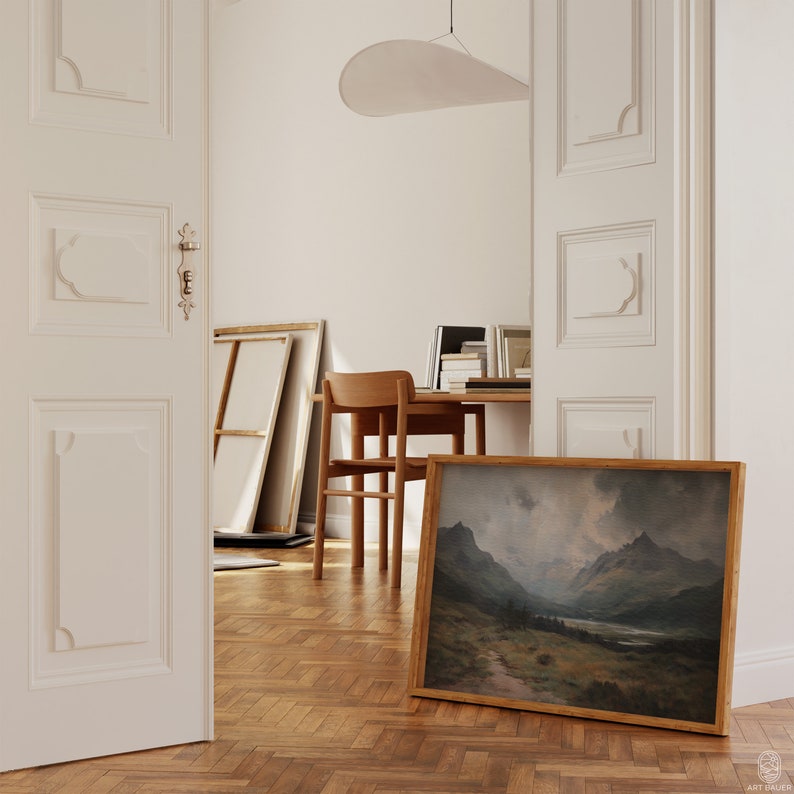 Pu&ograve; includere: Un dipinto di paesaggio incorniciato che rappresenta una catena montuosa con un lago in primo piano. Il dipinto &egrave; in una cornice di legno ed &egrave; appeso a una parete bianca.