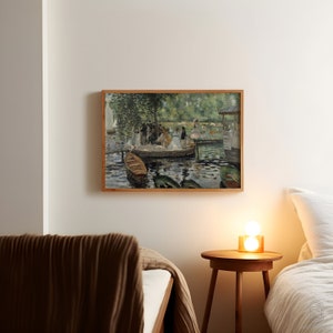 Op de afbeelding: Een ingelijst schilderij van een groep mensen in boten op een meer. Het schilderij is in een licht houten lijst en hangt aan een witte muur. Er is een bruin deken op een bed op de voorgrond.