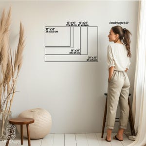 May include: A white wall with black text showing different sizes of canvas prints in inches and centimeters. The text includes "Female height is 65" inches. A person is standing in front of the wall, facing the canvas sizes.