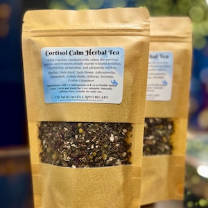 May include: Two brown paper pouches of Cortisol Calm Herbal Tea. Each pouch has a clear window showing the tea blend. The label includes the tea's ingredients: Rooibos, Holy Basil, Chamomile, and more. The text also includes instructions for use.