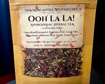 May include: A brown paper pouch with a label that reads "THE MERCANTILE APOTHECARY OOH LA LA! APHRODISIAC HERBAL TEA ~ CAFFEINE FREE ~" and lists the ingredients as "Damiana Leaf, Cacao Nibs, Honeybush, Hibiscus, Rose Petals, Ginger Root". The pouch contains a blend of dried herbs and rose petals.