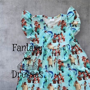 May include: A light blue dress with a print of cartoon characters. The dress has short sleeves with ruffled edges and a round neckline. The words "Fantasy Dresses" are printed on the front of the dress.