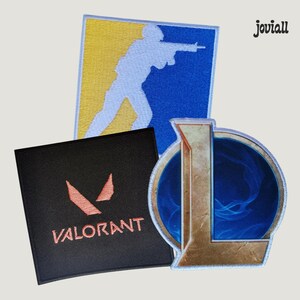 Op de afbeelding: Drie geborduurde gaming patches. Eén heeft een blauw en geel ontwerp met een wit silhouet van een persoon met een geweer. Een andere is zwart met het woord "VALORANT" en een rood logo. De derde patch heeft een blauwe achtergrond met een gouden letter "L".