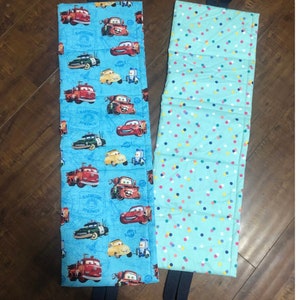 Op de afbeelding: Twee blauwe stoffen opbergbakken met handvatten. Een bak heeft een Cars-print met de tekst "Radiator Springs" en de andere bak heeft een kleurrijk stippenpatroon.