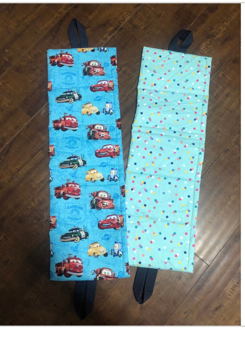Op de afbeelding: Twee blauwe stoffen opbergbakken met handvatten. Een bak heeft een Cars-print met de tekst "Radiator Springs" en de andere bak heeft een kleurrijk stippenpatroon.