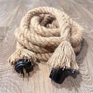 May include: A coiled, thick rope light cord with a natural, tan color. The cord has a decorative tassel at each end, with a black plug and socket. The cord is designed for use as a light fixture.