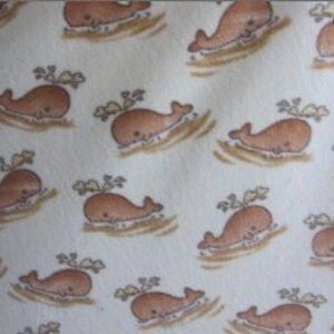 May include: A repeating pattern of cartoon whales in shades of brown and tan on a cream background. Each whale is depicted swimming with a small spray of water above it. The design is simple and whimsical.