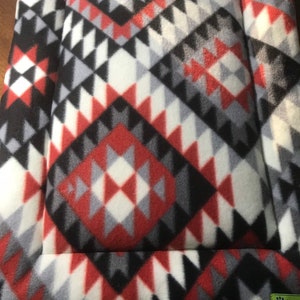 May include: A red, black, white and grey patterned pet bed with a raised border. The bed has a paw print logo with the text "Sherpa" on the bottom right corner.