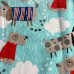 May include: A light blue fleece fabric featuring cartoon dogs wearing sweaters and coats. The dogs are in various poses, with white cloud and rain drop patterns. The dogs' outfits are red, blue, and white.