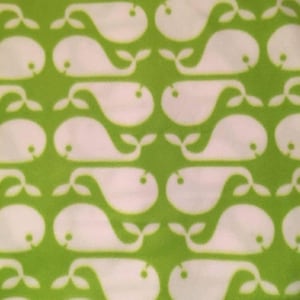 May include: A repeating pattern of white whales on a bright green background. The whales are stylized with a rounded body, a small eye, and a curved tail. The design is simple and playful, suitable for children's items or nautical-themed decor.