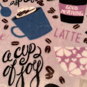 May include: A light purple blanket with coffee-themed designs. The blanket features coffee cups, coffee beans, and the words "espresso", "latte", and "a cup of joy". A coffee cup has the words "Good Morning" on it.
