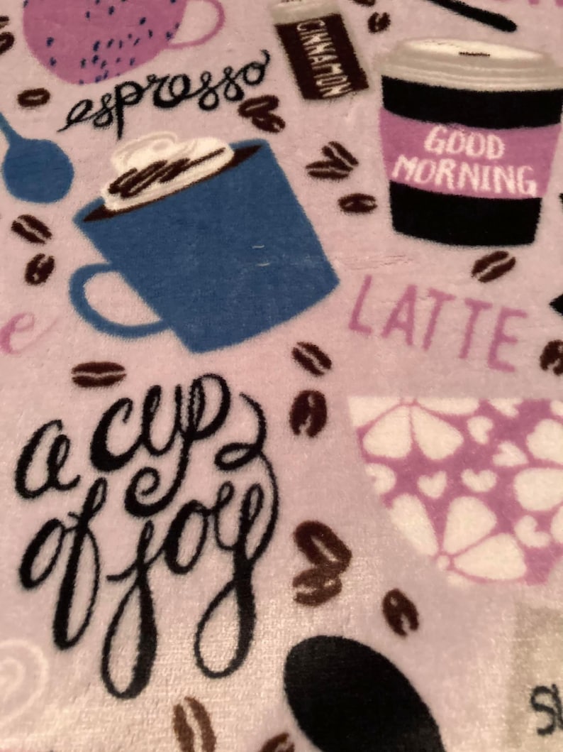 May include: A light purple blanket with coffee-themed designs. The blanket features coffee cups, coffee beans, and the words "espresso", "latte", and "a cup of joy". A coffee cup has the words "Good Morning" on it.