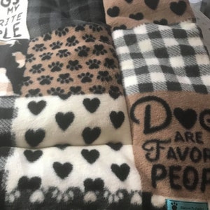 May include: A multi-colored patchwork dog bed with a brown fabric panel that reads "Dogs are my favorite people". The bed is made of soft fleece and has a variety of patterns, including paw prints, hearts, and plaid.