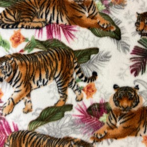 May include: A white fabric with a repeating pattern of tigers, orange flowers, and green and pink tropical leaves. The tigers are orange and black, and some are lying down while others are standing.