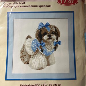 May include: A RIOLIS 1120 cross stitch kit featuring a brown and white dog wearing a blue polka dot outfit with three blue ribbons. The packaging displays the text RIOLIS, Create it Yourself, 1120, and a finished size of 9 3/4 inches by 9 3/4 inches.