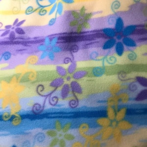 Può includere: Un tessuto colorato con un motivo a righe e disegni floreali in tonalità di blu, giallo, verde e viola.