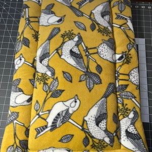 May include: A yellow pet bed with a white and gray bird pattern. The bed has a black border and a small blue tag that says "Sharing Pet Comfort".