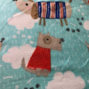 May include: A light blue fleece fabric featuring a repeating pattern of cartoon dogs, white clouds, and paw prints. The dogs are in various colors, including brown, gray, and white, and wear red or striped sweaters.