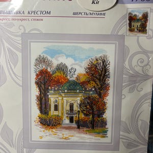 May include: A Riolis cross stitch kit 1760 featuring a printed design of the Kuskovo Hermitage estate. The image shows a yellow building with a green dome surrounded by autumn trees in shades of orange, red, and brown. The kit measures 18 x 22 cm.