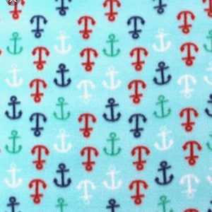 May include: A light blue fabric with a repeating pattern of anchors in red, navy blue, green, and white. The anchors are evenly spaced across the fabric, creating a nautical theme.