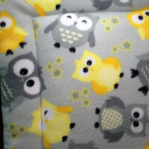 May include: A grey pet bed featuring a repeating pattern of yellow and grey owls and yellow stars. The owls have white eyes and black pupils. The bed has a stitched border.