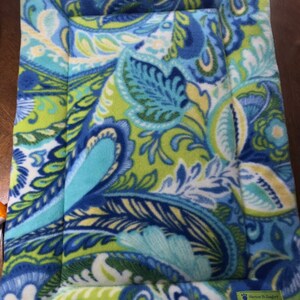 May include: A blue, green, and white paisley patterned pet bed with a light blue border. The bed has a label that reads "Moments to Snuggles".