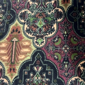 May include: Close-up of a patterned textile featuring an intricate design. The pattern includes floral and geometric shapes in shades of green, purple, beige, and navy blue. The textile has a soft, plush appearance, suggesting a rug or fabric.