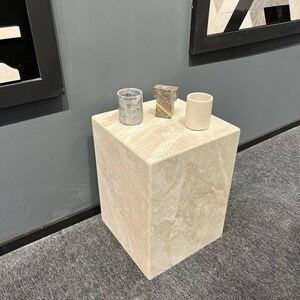 Puede incluir: Un peque&ntilde;o pedestal cuadrado de m&aacute;rmol beige claro con una copa de m&aacute;rmol gris y blanco, una copa de m&aacute;rmol gris y dorado y una copa de m&aacute;rmol blanco en la parte superior.
