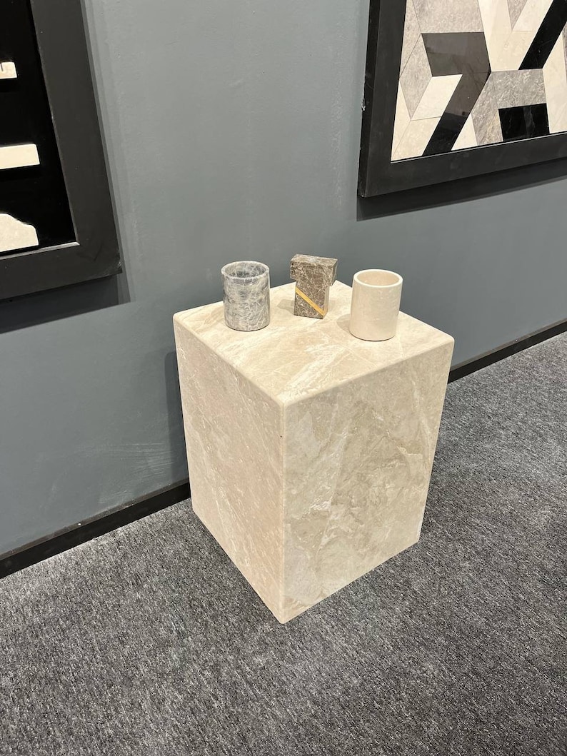 Puede incluir: Un peque&ntilde;o pedestal cuadrado de m&aacute;rmol beige claro con una copa de m&aacute;rmol gris y blanco, una copa de m&aacute;rmol gris y dorado y una copa de m&aacute;rmol blanco en la parte superior.