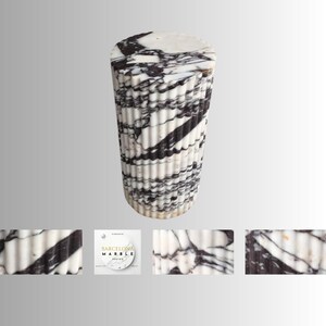 May include: A cylindrical marble accent table with a fluted design. The table features a white and black veined pattern. The top is a solid white marble. The table is approximately 18 inches tall.