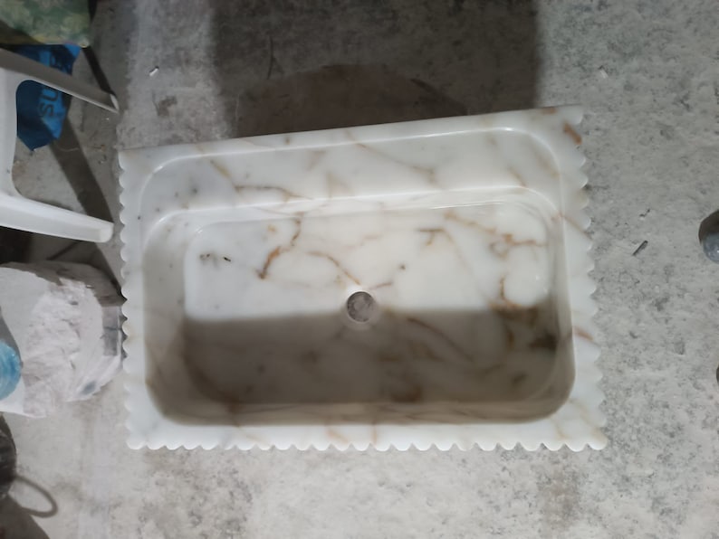 May include: White marble sink with a scalloped edge and a drain hole in the center. The sink has a light brown veining pattern.