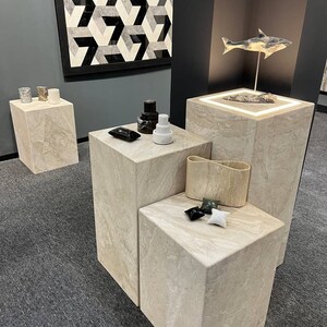 Puede incluir: Cuatro pedestales de m&aacute;rmol beige con varios objetos en la parte superior, incluyendo un azulejo geom&eacute;trico en blanco y negro, una escultura de pez en blanco y negro, un candelero en blanco y negro y una escultura de piedra en blanco y negro.