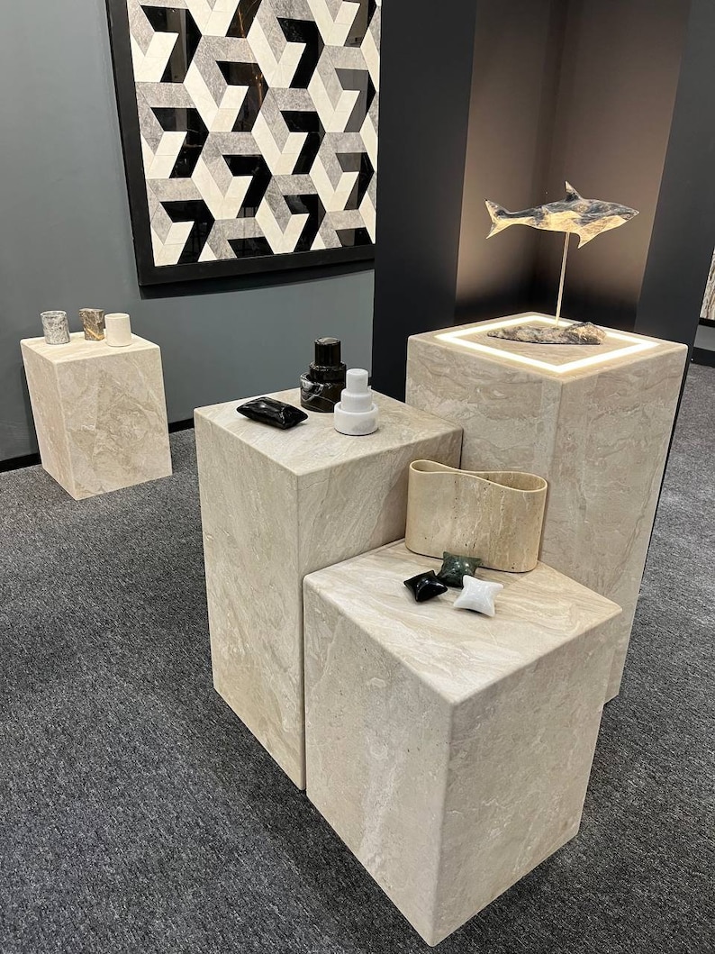Puede incluir: Cuatro pedestales de m&aacute;rmol beige con varios objetos en la parte superior, incluyendo un azulejo geom&eacute;trico en blanco y negro, una escultura de pez en blanco y negro, un candelero en blanco y negro y una escultura de piedra en blanco y negro.