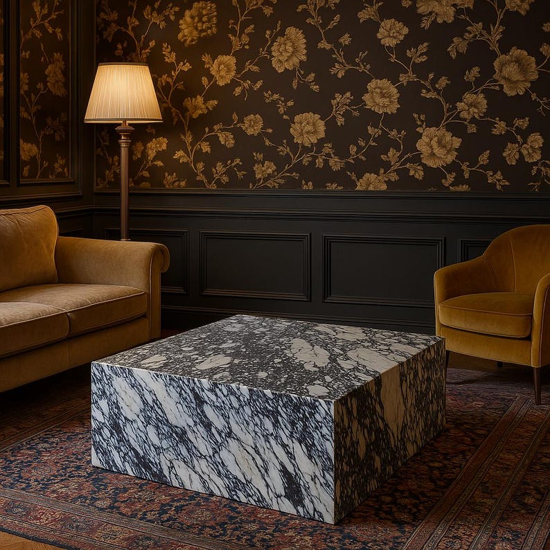 K&ouml;nnte beinhalten: Ein quadratischer Couchtisch aus schwarz-wei&szlig;em Marmor mit einem dunkelbraunen Teppich mit Muster darunter. Der Tisch steht in einem Raum mit einer braunen Tapete mit Muster, einem braunen Sofa und einem braunen Sessel.