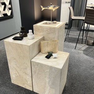 Puede incluir: Tres pedestales de cubo de piedra beige con una escultura de tibur&oacute;n blanco y negro en el pedestal superior. Los pedestales est&aacute;n sobre una alfombra gris.
