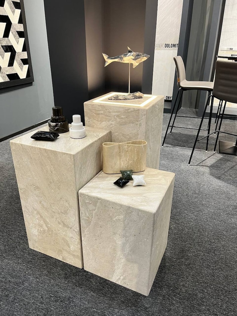 Puede incluir: Tres pedestales de cubo de piedra beige con una escultura de tibur&oacute;n blanco y negro en el pedestal superior. Los pedestales est&aacute;n sobre una alfombra gris.