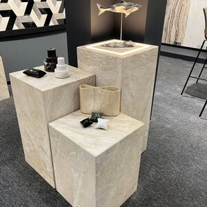 Puede incluir: Tres expositores de piedra beige con una escultura de pez de madera en el expositor superior. Los expositores est&aacute;n sobre una alfombra gris.