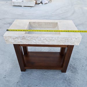 May include: A rectangular beige stone sink with a rough-hewn front edge, mounted on a dark brown wooden vanity base with a lower shelf. A yellow measuring tape is stretched across the top, showing a width of approximately 45 inches.