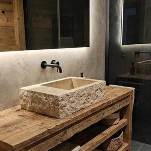 May include: A bathroom vanity featuring a rectangular stone sink and black tap. The sink is set on a reclaimed wood cabinet with open shelving. The mirror has integrated lighting. The design is natural and minimalist, with a focus on texture.