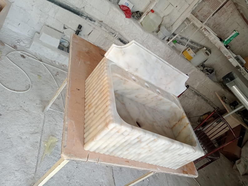 May include: A white marble sink with a decorative, fluted design. The sink is mounted on a wooden table.