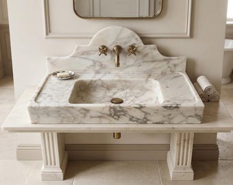May include: A marble bathroom sink with a rectangular basin and a decorative backsplash. The sink has a brass faucet and is mounted on a matching marble stand. A small soap dish and rolled towels are on the counter. The room has a classic, elegant design.