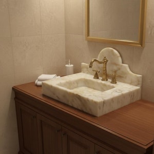 Puede incluir: Un lavabo de m&aacute;rmol con grifos dorados se encuentra sobre un mueble de ba&ntilde;o de madera oscura. El lavabo tiene una pila rectangular y un protector contra salpicaduras decorativo. Un espejo con marco dorado cuelga sobre el lavabo.