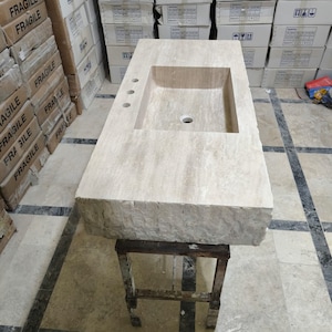 May include: A rectangular beige travertine stone bathroom vanity top featuring a single integrated rectangular sink basin, a smooth polished top surface, and a rough-hewn natural rock edge. The vanity includes three pre-drilled faucet holes.