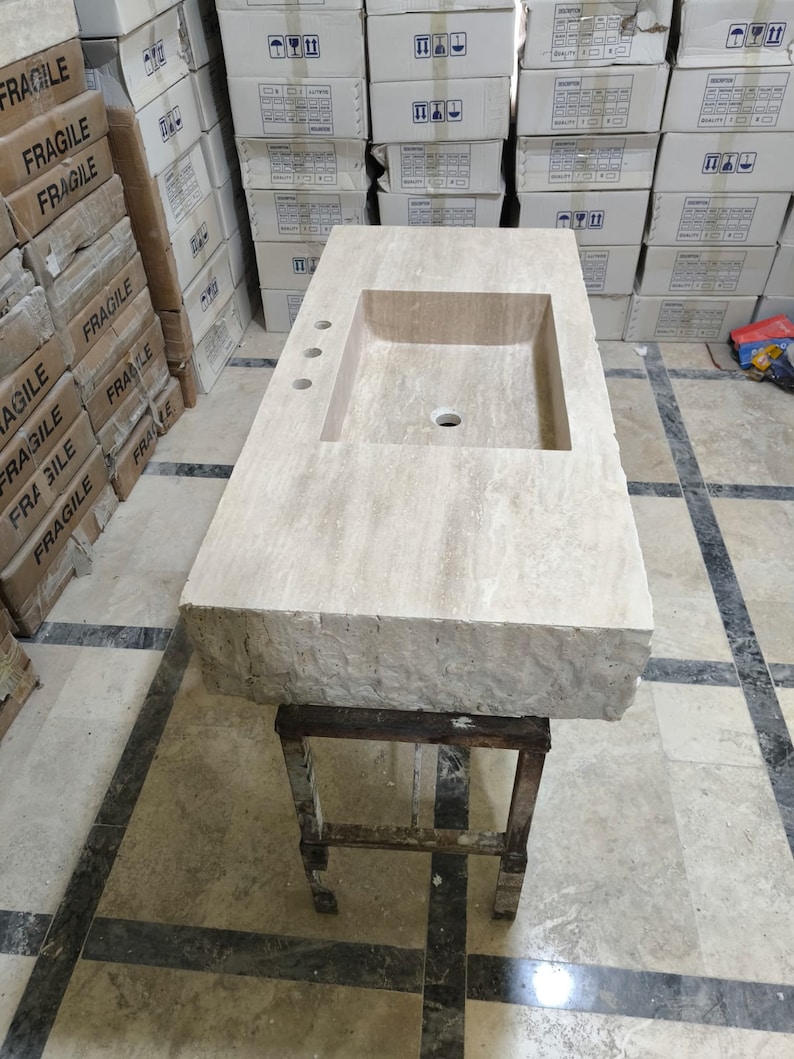 May include: A rectangular beige travertine stone bathroom vanity top featuring a single integrated rectangular sink basin, a smooth polished top surface, and a rough-hewn natural rock edge. The vanity includes three pre-drilled faucet holes.