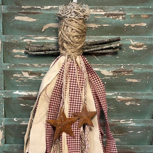 May include: A handmade rag wreath with red and white gingham fabric, beige fabric, and brown twine. Two rusty metal stars are attached to the wreath.
