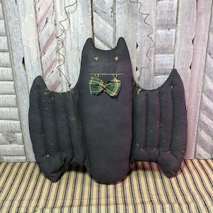 May include: A black fabric bat with green and gold plaid bow tie hanging from a wire loop. The bat is handmade and has a rustic, primitive style.