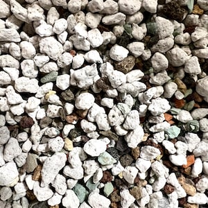 May include: A collection of small, porous volcanic rocks in various shades of white, light gray, dark brown, and pale green. The stones have an irregular, jagged texture with visible holes and crevices, creating a dense, multi-colored aggregate.